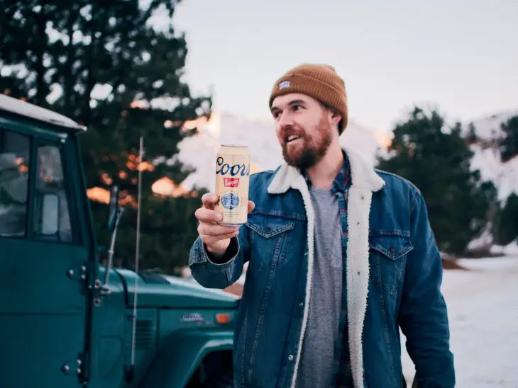 man in blue denim jacket holding Coors Yellowjacket