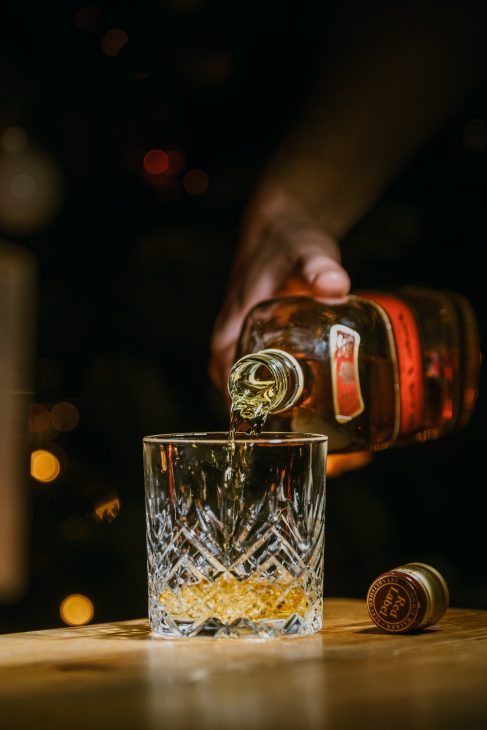 person holding clear drinking glass with brown liquid