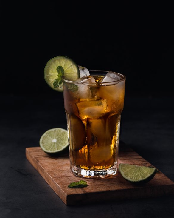 Rum vs whiskey - a glass filled with an amber alcohol, ice, and lime.